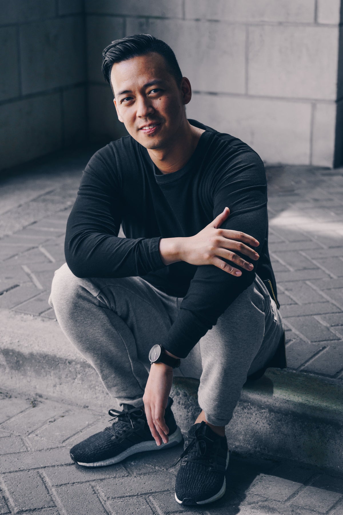 Man in a black long-sleeve tee and grey joggers sitting on a step