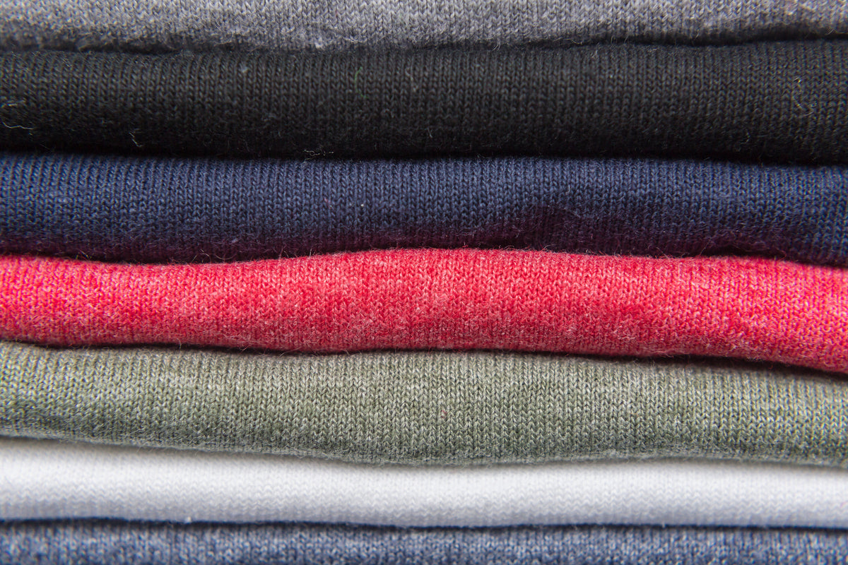 A neat stack of folded knit sweaters in soft muted colours