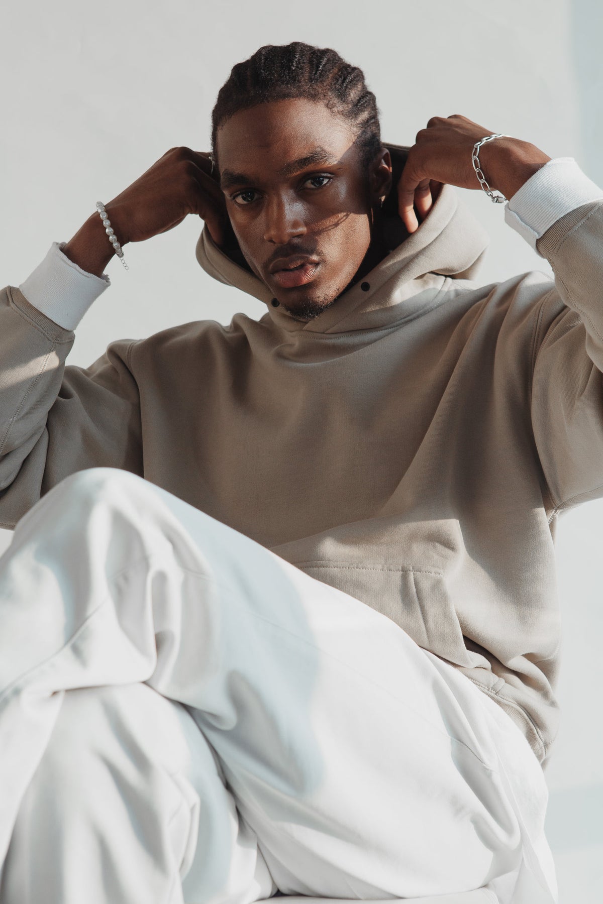 Man in a taupe oversized hoodie and white trousers