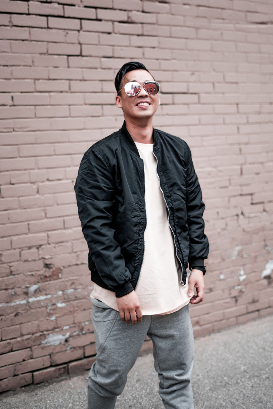 Man in a black bomber jacket and grey joggers against a brick wall