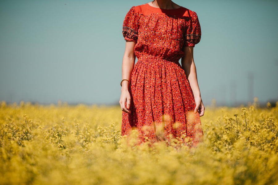 Woman in a red floral midi dress standing in a yellow field